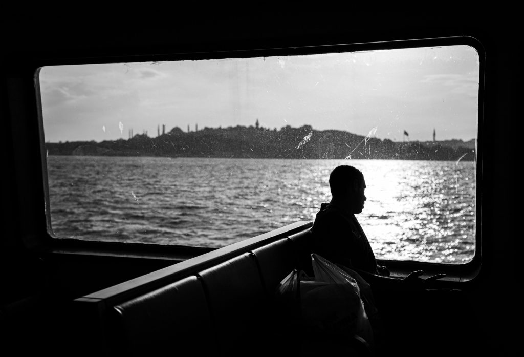Black and white photo of a silhouette on an Istanbul ferry with a view of the skyline and sea.